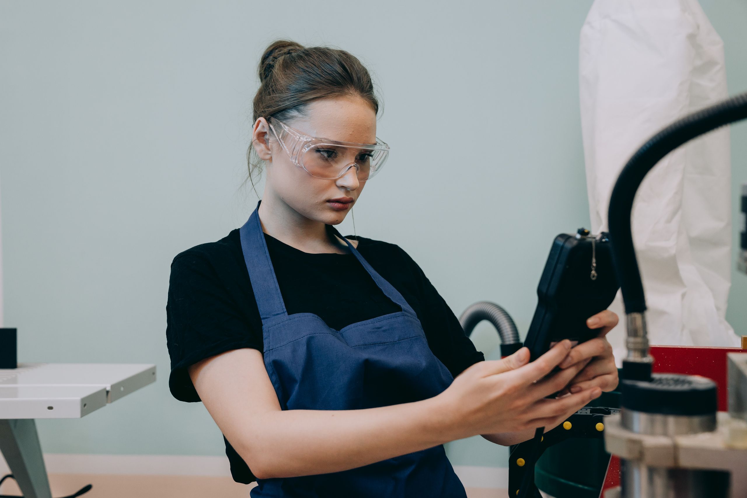 A woman in a blue apron uses a device in a workshop wearing protective goggles. 9241695 scaled